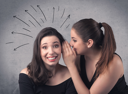 A cute teen caucasian girl telling secret things to her girlfriend dressed in black dress concept with drawn lines, curves, spirals on grey wall background.の写真素材