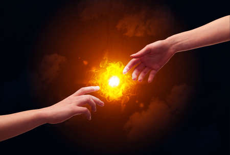 Two naked male hands about to touch, lighting a bright flame with smoke in red sky background conceptの写真素材