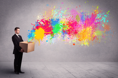 A young smiling business male holding a paperboard box with illustration of colourful spray paint splash on urban wall background concept.の写真素材