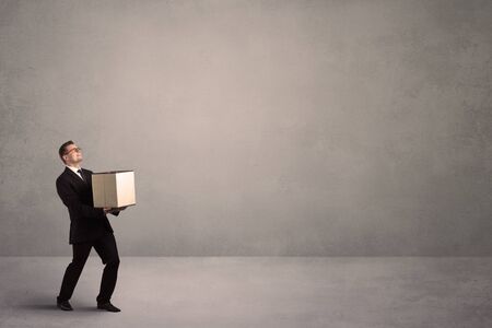 A well dressed young office worker holding an empty paper box with clear concrete wall background concept.の写真素材
