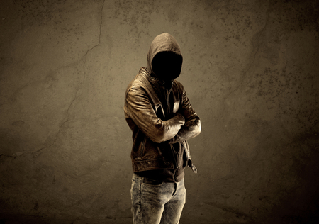 A suspicious faceless mature male in dark urban environment and light in front of a concrete empty wall backgroundの写真素材