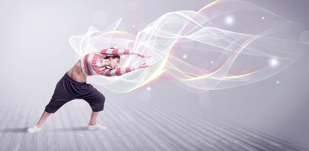 A beautiful young hip hop dancer dancing contemporary urban street dance in front of grey wall background with smokey lines and glitter concept.の写真素材