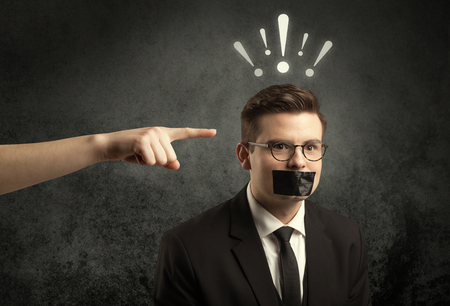 Caucasian hand pointing at employee in business suit, with drawn exclamation marks above his headの写真素材