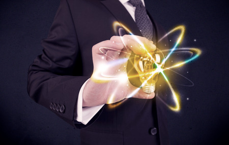 A classy businessman holding a colorful light bulb with shining circles in front of dark background concept.の写真素材