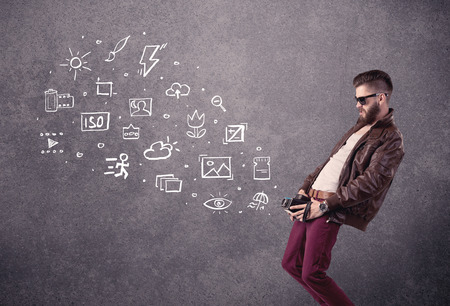An elegant hipster guy trying to use a vintage camera with camera settings icons drawn on wall, like flash, white balace or ISO value conceptの写真素材