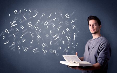 Casual young man holding book with white letters flying out of itの写真素材
