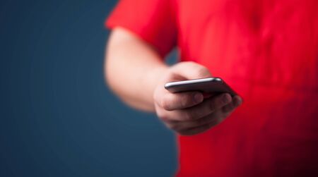 Young man holding smarthphone in hand while typingの写真素材