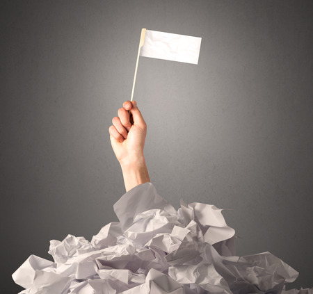 Female hand emerging from crumpled paper pile holding a white blank flagの写真素材
