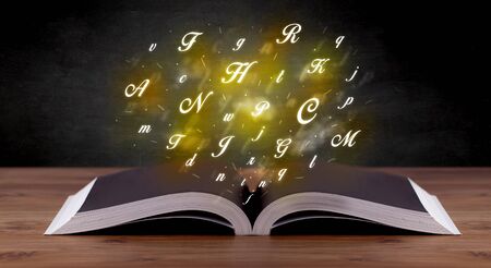 Glowing yellow alphabet letters coming out of an open bookの写真素材