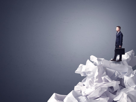 Thoughtful young businessman standing on a pile of crumpled paper with a dark grey backgroundの写真素材