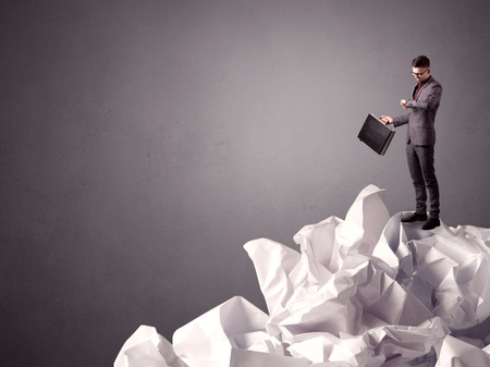 Thoughtful young businessman standing on a pile of crumpled paper with a grungy grey backgroundの写真素材