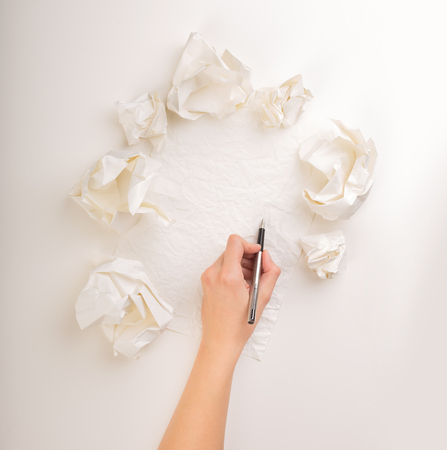 Female hand trying to write next to a few crumpled paper ballsの写真素材