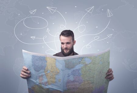 Handsome young man holding a map with drawn paper planes flying behind him