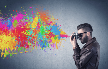 A retro hipster male taking photograph with a vintage camera of an urban wall with paint splatter conceptの写真素材