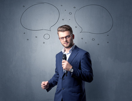 Businessman speaking into microphone with speech bubbles over his headの写真素材