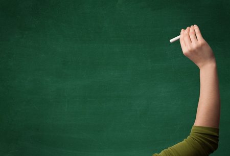 A mature hand writing or drawing on a clean green blackboard with a white chalk.の写真素材