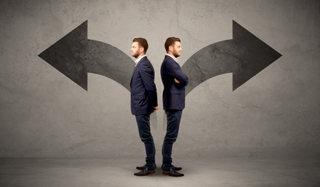 Young conflicted businessman choosing between two directions represented by black arrowsの写真素材