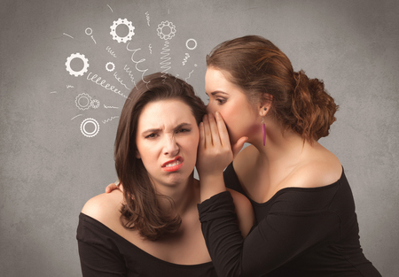 Two girlfriends in elegant black dress sharing secrets with each other concept with drawn rack cog wheels and spiral lines on the wall background.の写真素材