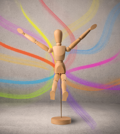 Wooden mannequin posed in front of a greyish background with colorful lines behind itの写真素材
