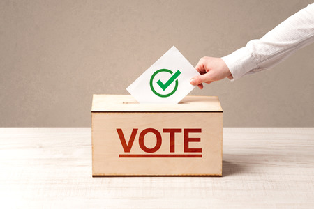 Close up of male hand putting vote into a ballot box, on grunge backgroundの写真素材