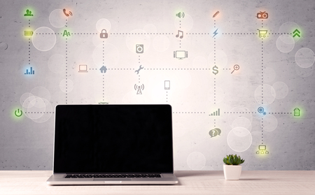 Notebook with blank screen sitting on office desk in front of background wall full of communication icons and illustrated connections conceptの写真素材