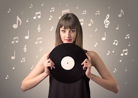Young lady holding vinyl record on a brown background with musical notes behind herの写真素材