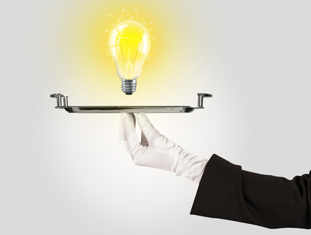 Serving a bright business idea concept using a bulb with bright sparkling warm yellow light presented on a silver plateの写真素材