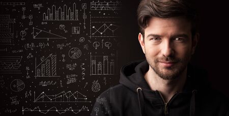 Portrait of a young businessman with charts and graphs scribbled next to him on a dark backgroundの写真素材