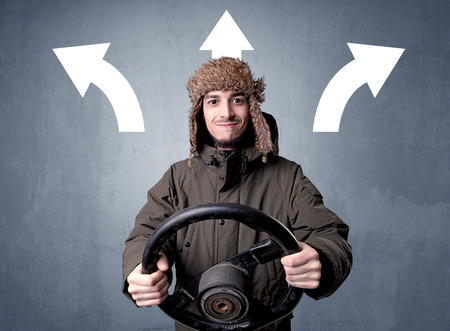 Young man holding black steering wheel with three arrows above his head pointing in different directionsの写真素材