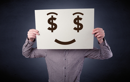 Young casual businessman hiding behind a greedy face drawing on cardboardの写真素材