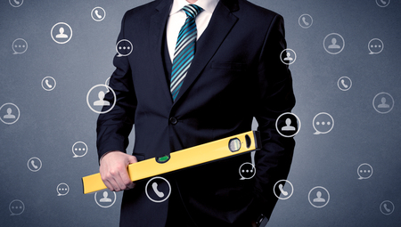 Thoughtful businesman holding tool with communication symbols aroundの写真素材