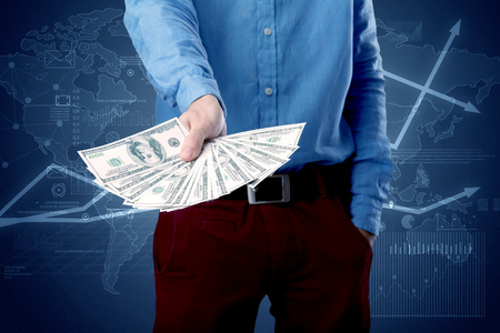 Young businessman holding large amount of bills with blue charts in the backgroundの写真素材
