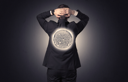 Businessman standing and thinking with maze graphic on his backの写真素材