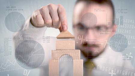 Young handsome businessman using wooden building blocks with data and numbers around him