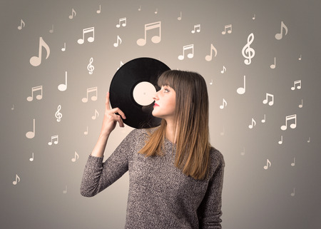 Young lady holding vinyl record on a brown background with musical notes behind herの写真素材