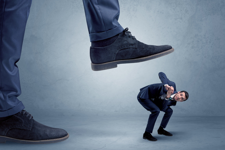 Young small businessman is trampled by a big foot in an empty spaceの写真素材