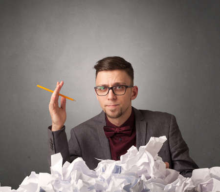 Young businessman sitting behind crumpled paper with grey backgroundの写真素材