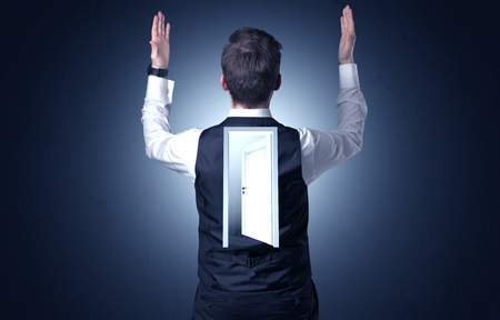Young businessman standing and thinking with an open door on his backの写真素材