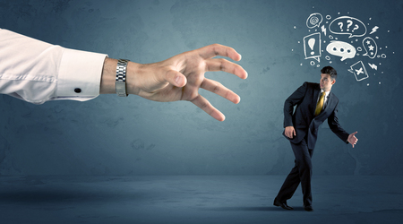 Business man with doodle icons running from a big hand concept on backgroundの写真素材