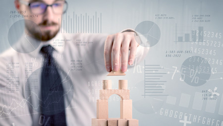 Young handsome businessman using wooden building blocks with data and numbers around him