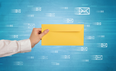 Female hand holding coloured and white envelope with blue background and message symbols aroundの写真素材