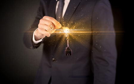 Businessman hand  over shiny keys in dark suit with dark backgroundの写真素材