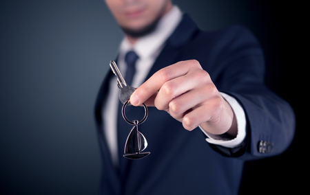 Young businessman hand over keys with empty dark backgroundの写真素材