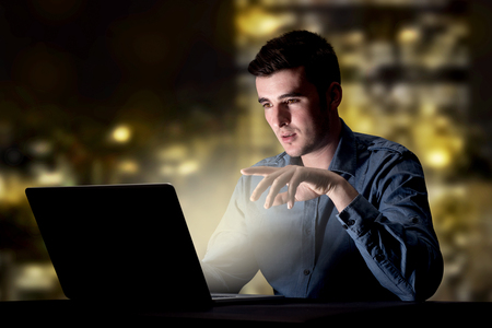 Young handsome businessman working late at night in the office with city lights in the backgroundの写真素材