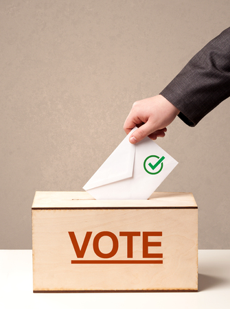 Close up of male hand putting vote into a ballot box, on grunge backgroundの写真素材