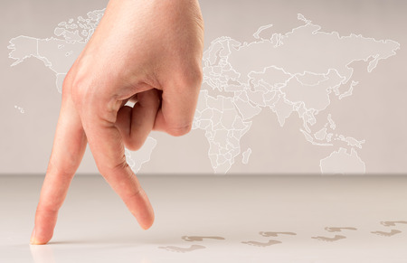 Female fingers walking with footsteps behind them and a world map in the backgroundの写真素材