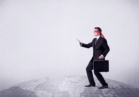 Young blindfolded businessman steps on a grey world mapの写真素材