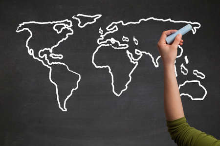 A teacher drawing the map of the world on a blackboard with a chalkの写真素材