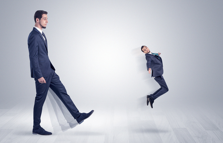 Big man in suit kicking out little himself with simple white wallpaper
の写真素材