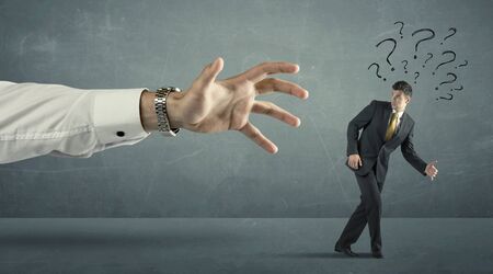 Businessman with question marks running away from a big hand concept on backgroundの写真素材